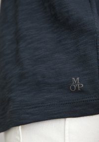 Himmelblaues Kurzarmhemd aus strukturiertem Stoff, mit einem kleinen "MOP"-Logo in Beige am Saum, entworfen für Freizeitkleidung.