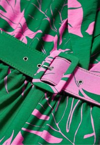Abito di stoffa verde con motivi a foglia rosa. Presenta una ampia cintura rosa con una fibbia in metallo e fori per la regolazione. Texture liscia.