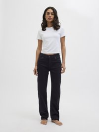 Σκούρα τζιν παντελόνια με ίσια γραμμή και ψηλή μέση, με λεπτομερή ραφή και σχέδιο πέντε τσεπών, φορεμένα με ένα απλό λευκό μπλουζάκι με στρογγυλή λαιμόκοψη.