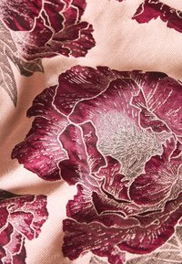 Ciemny bordowy wzór kwiatowy na jasnoróżowej, teksturowanej tkaninie, z detalami płatków i liści o subtelnym połysku i kontraście.