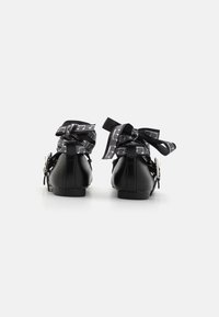 Black leather ankle boots with a rounded toe and flat heel. Decorative black and white musical note ribbons tied at the back. Silver hardware accents.