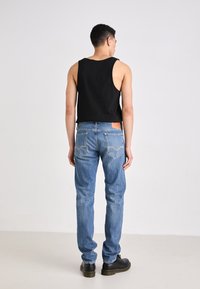 Zwarte mouwloze tanktop gecombineerd met lichtblauwe denim jeans. De jeans hebben een gestikt zakontwerp en een bruine leren label aan de taille.