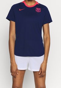 Marinblå Nike fotbollsjacka med rosa krage och detaljer, med Barcelonas klubbmärke på bröstet. Lättviktig, kortärmad design.