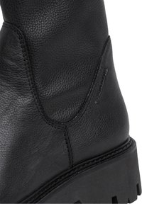 Botín de cuero negro hasta el tobillo con acabado texturizado, detalles cosidos y suela de goma negra gruesa. Presenta un panel lateral y una sutil marca.