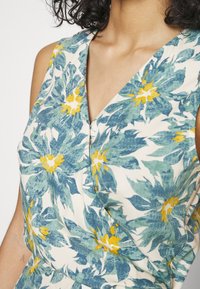 Robe fleurie avec un décolleté en V, fabriquée en tissu léger avec des motifs de fleurs bleues et jaunes sur un fond crème.