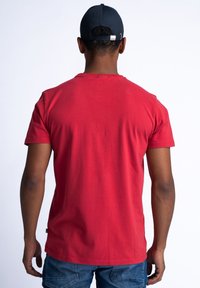 Red cotton t-shirt with short sleeves and a round neckline, featuring a smooth texture and a logo tag at the hem.