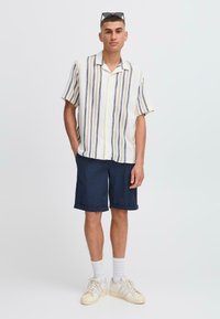Korte ermer, knappet skjorte med flerfargede striper, kombinert med marineblå shorts og hvite joggesko, med brettede mansjetter og teksturert stoff.
