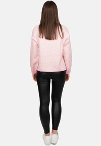 Maglione a stampa leopardata rosa con maniche lunghe, abbinato a leggings neri lucidi e sneaker bianche, visto di spalle.