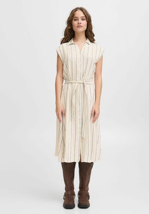 Creme-farbenes, knielanges Kleid mit vertikalen marineblauen Streifen, kurzen Ärmeln, durchgehender Knopfleiste und einem gebundenen Taillengürtel, kombiniert mit braunen Stiefeln bis zum Knie.