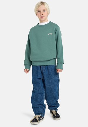 Grüner Sweatshirt mit Rippbündchen und Saum, mit "BILLABONG"-Logo. Kombiniert mit lockeren blauen Jeans und schwarzen Sneakers.