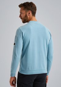 Hellblaues Sweatshirt mit langen Ärmeln, Rundhalsausschnitt, gerippten Bündchen und Taillenbund. Verfügt über eine Taschen auf dem linken Ärmel.