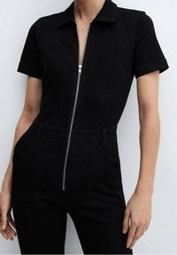 Černý denims overal s krátkými rukávy, úzkým střihem a předním zipem. Obsahuje klasický límec a minimalistický design.