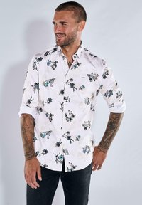 Weißes Button-Down-Hemd mit floralem Muster in Blau- und Schwarztönen, mit umgeschlagenen Ärmeln und abgerundetem Saum. Aus Baumwollstoff, lockere Passform.