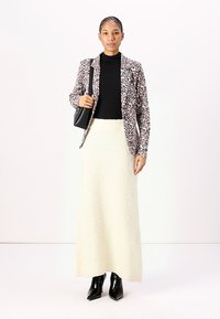 Blazer s leopardím potiskem, černý rolák, bílá texturovaná maxi sukně a černé vysoké boty na podpatku. Modelka drží černou kabelku.