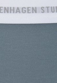 Harmaan sininen kangas, jossa on tekstuuri, ja yläreunassa valkoinen nauha, jossa lukee harmaalla "COPENHAGEN STUDIOS".