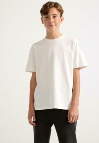T-shirt bianco a maniche corte in cotone, con scollatura rotonda e vestibilità comoda, abbinato a jeans di denim scuro.
