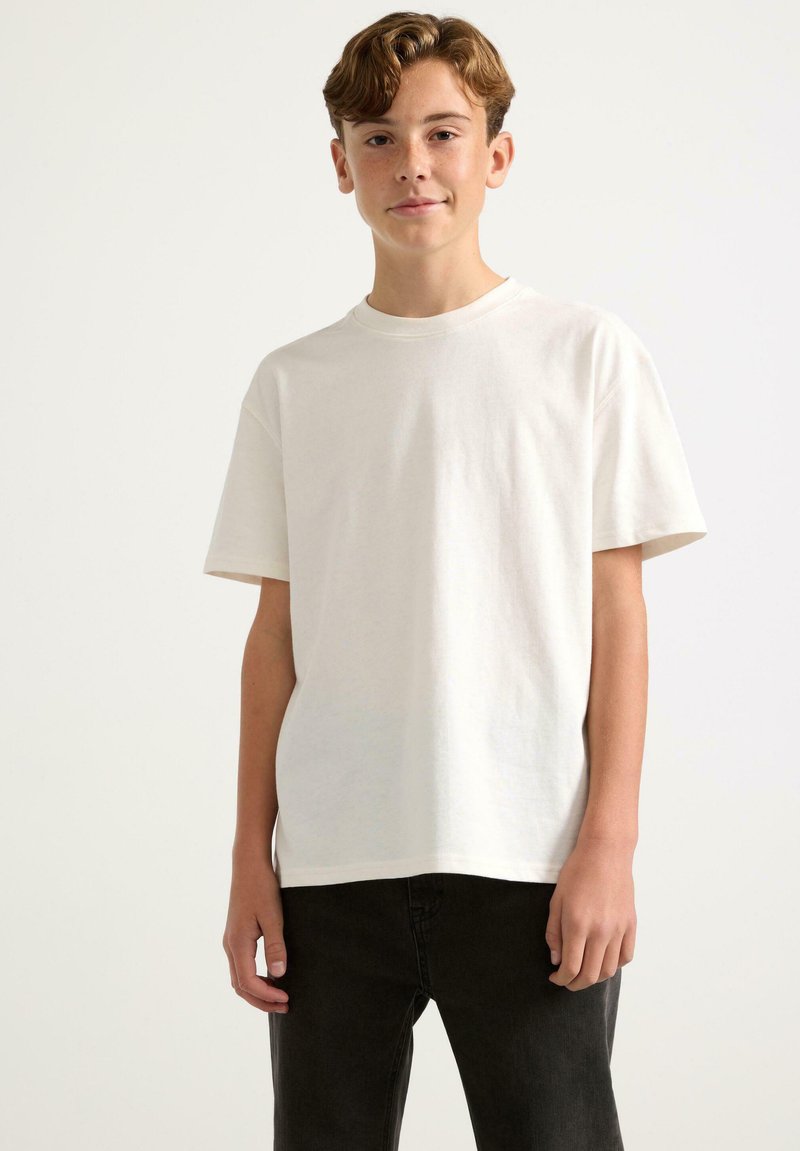 T-shirt bianco a maniche corte in cotone, con scollatura rotonda e vestibilità comoda, abbinato a jeans di denim scuro.