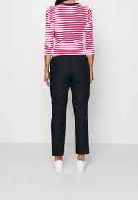 Maglietta a maniche lunghe a righe rossa e bianca abbinata a pantaloni neri; modello che indossa sneakers bianche, visto da dietro. Tessuto liscio, design aderente.