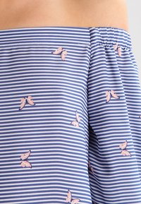 Modro-bílá pruhovaná látka s malými vzory růžových motýlků. Materiál vypadá lehký a měkký, s elastickým pasem.