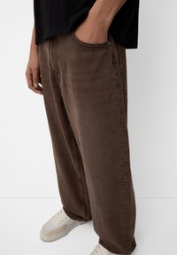 Brown wide-leg pants made of soft cotton denim with a front pocket and a textured finish, paired with light-colored sneakers.