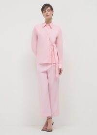 Blusa rosa chiaro con dettaglio incrociato in vita e chiusura con bottoni. Abbinata a pantaloni a gamba larga rosa chiaro e sandali con tacco neri.