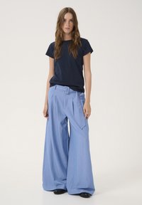 Marineblaues T-Shirt und hellblaue, gestreifte, weit geschnittene Hosen mit einem Gürtel. Die Hosen haben Falten und Seitentaschen, der Stoff wirkt glatt.