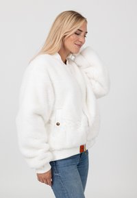 Weiße Kunstpelz-B bomberjacke mit geripptem Kragen und Bündchen, Fronttaschen und strukturiertem Finish, kombiniert mit hellblauen Jeans.