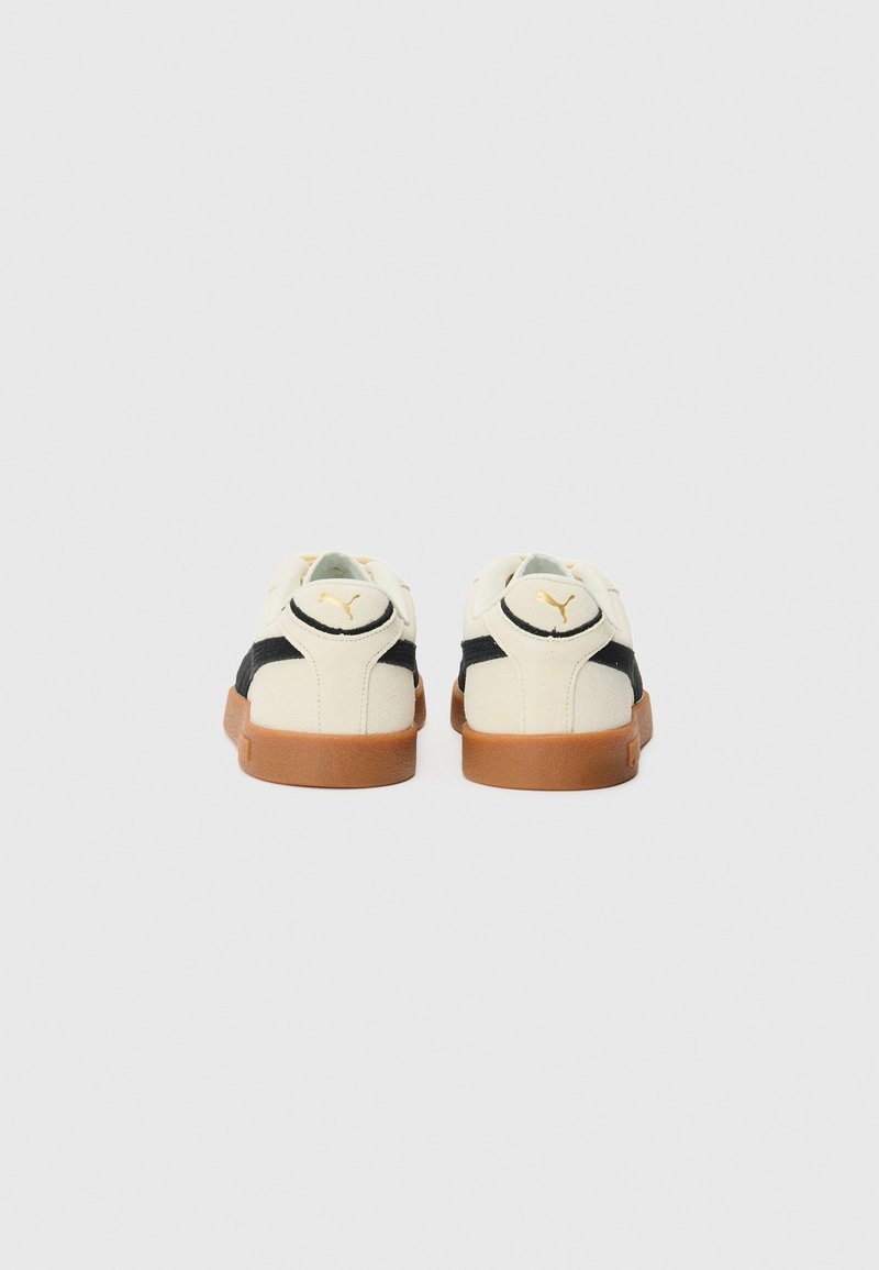 Baskets blanches et noires avec une semelle en caoutchouc beige, présentant un dessus en tissu texturé et un accent de logo sur le talon. Forme de pied arrondie.