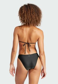 Svart bikini med halterneck-design, knytbakslutning och lågriskjol. Slät material med minimal branding på midjebandet.