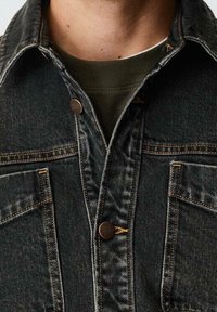 Chaqueta de mezclilla oscura con cierre de botones en el frente, dos bolsillos en el pecho, detalles de costura en naranja y un diseño de cuello clásico.