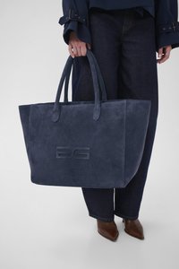 Laivastonsininen mokkanahkainen olkalaukku, jossa on kaksi kahvaa ja etupuolella painettu logo. Sileä pinta ja jäsennelty muoto, sopii päivittäiseen käyttöön.