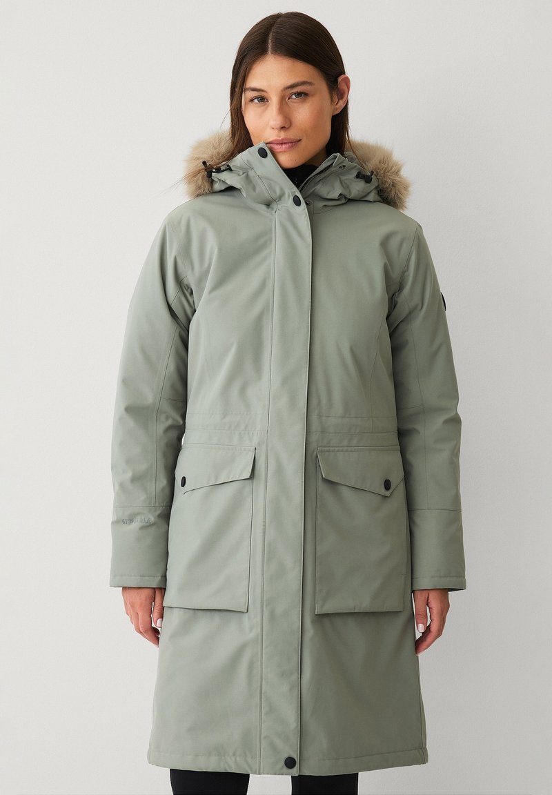 Lichtgroene parka met een met bont gevoerde kap, ritssluiting, twee grote voorzakken en een knielange pasvorm. Gladde, waterdichte stof.