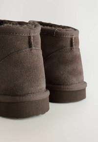 Bottines en suede marron avec doublure douce, présentant une vue rapprochée de l'arrière et des côtés, mettant en avant la texture et les détails de couture.