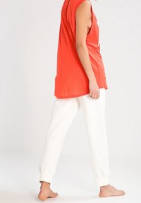 Ærmeløs orange top og hvide sweatpants med en løs pasform, blødt stof og ribbede manchetter ved anklerne. Enkel design uden mønstre.