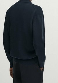 Marineblauwe geribbelde trui met hoge hals en relaxed fit. Heeft verlaagde schouders en een gestructureerd breipatroon.