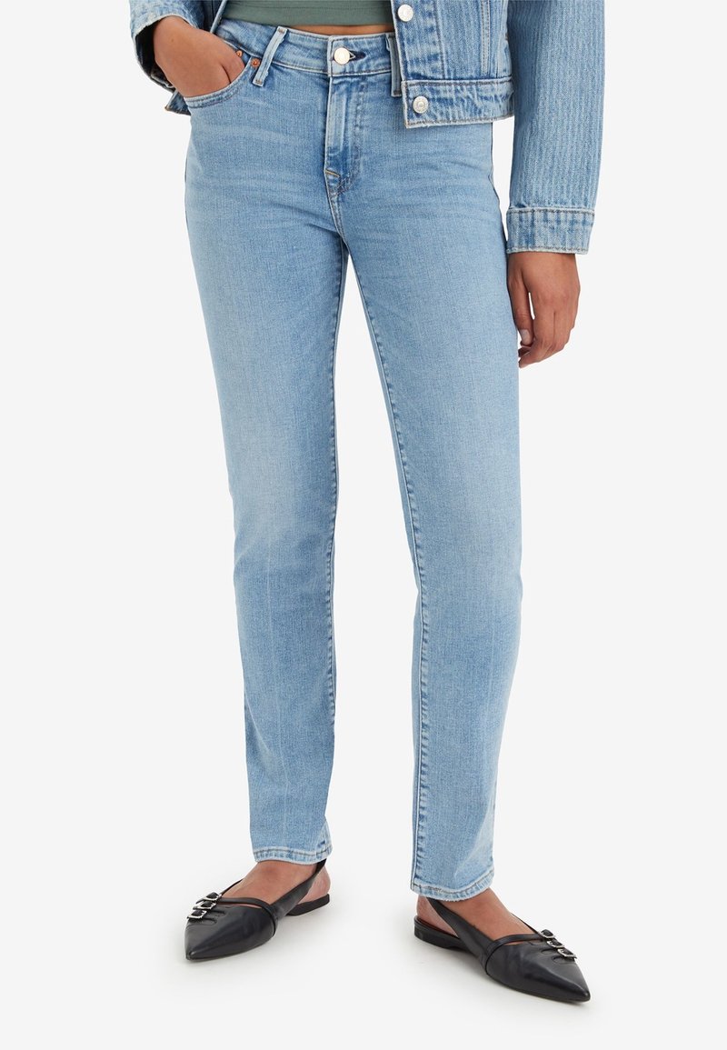 Personne portant un jean slim bleu clair, une veste en jean et des ballerines slingback noires à bout pointu avec des boucles.