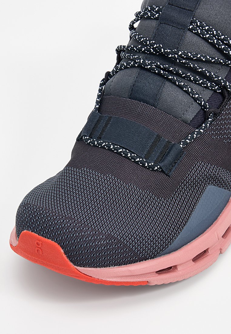 Close-up van een marineblauwe en roze sportshoe met gestreepte zwart-witte veters en een gestructureerde gebreide bovenkant.