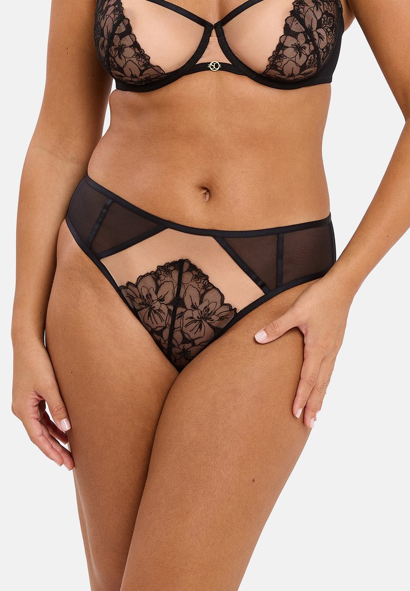 Ensemble de lingerie en dentelle noire avec motifs floraux, accents en maille et design découpé. Le tissu est transparent et léger, avec des éléments de soutien.
