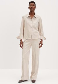 Camicia button-up beige a coste con colletto e maniche ampie, abbinata a pantaloni larghi in tinta. Tessuto texturizzato e design sottile.