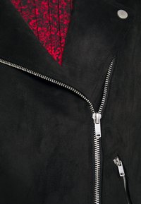 Giacca in suede nero con chiusura a zip diagonale e fodera floreale rossa. Include accessori metallici argentati e una tasca laterale con zip.