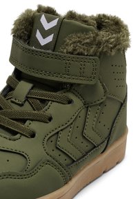 Olive zielone sneakersy za kostkę z futrzanym wykończeniem, sznurowaniem z przodu i paskiem na rzep. Posiadają akcenty w kształcie szewronu oraz gumową podeszwę z teksturowanym wykończeniem.