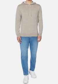 Beige hoodie med en ljusgrå innerfoder, dragband, som matchas med ljusblå jeans och vita sneakers.