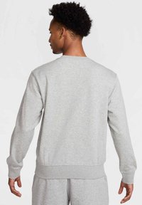 Grå sweatshirt lavet af blødt, tekstureret materiale med rund halsudskæring, ribbede manchetter og bærestykke. Har lange ærmer og en afslappet pasform.