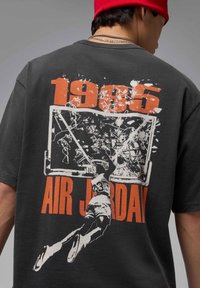 Black cotton t-shirt featuring a graphic print of a basketball player dunking, with "1985" and "AIR JORDAN" in bold orange letters.