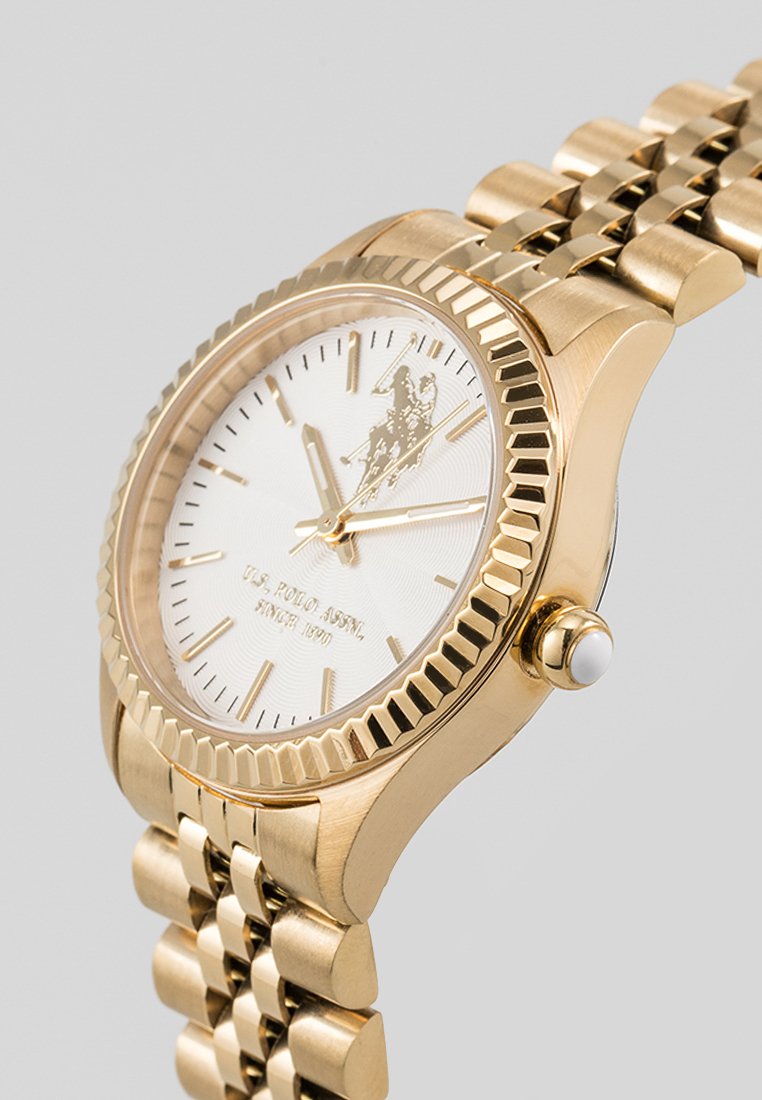 Orologio da polso dorato con quadrante bianco texturizzato, indicatori delle ore dorati e una lunetta scanalata. Presenta un bracciale in metallo dorato con chiusura.