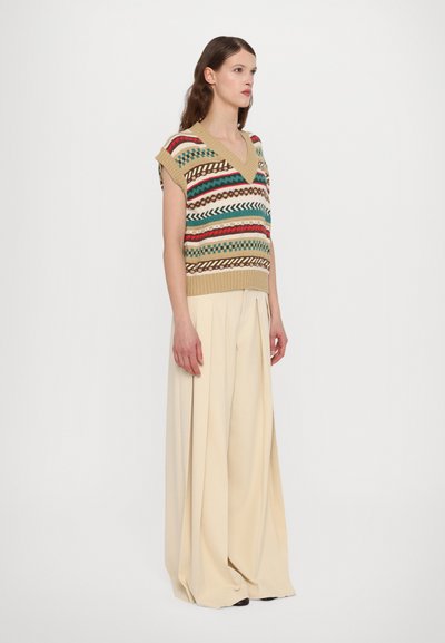 Top sin mangas de punto con escote en V en color beige, con patrones geométricos multicolores; combinado con pantalones anchos beige para un ajuste holgado.