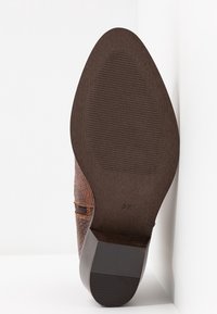 Suela de un zapato de vestir de cuero marrón con tacón texturizado y talla 37 marcada cerca del medio de la suela, sobre un fondo blanco.