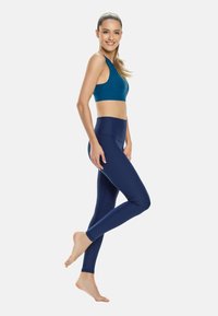 Top sportivo turchese e leggings blu navy, realizzati in materiale elasticizzato, dotati di vita alta e design senza cuciture, mostrando una texture e una vestibilità lisce.