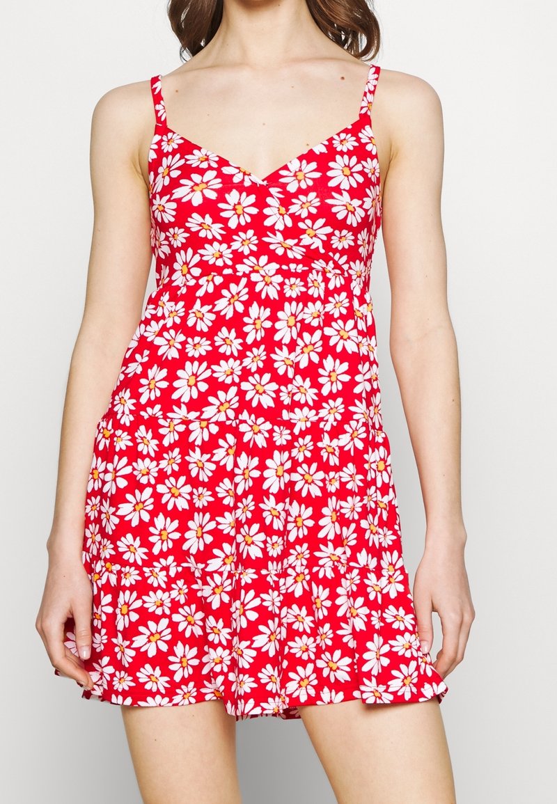 Röd ärmlös sommardress med vit och gul blommönster, åtsittande liv och utsvängd kjol. Gjord av lätt och andningsbart tyg.