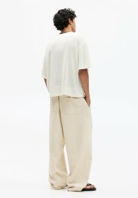 Relaxed-fit, short-sleeve, off-white top with a textured finish, paired with loose, beige, wide-leg trousers featuring back pockets.